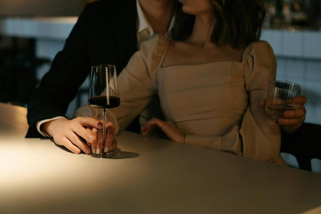 Woman in Beige Long Sleeve Shirt Holding Wine Glass with A Man Behind Her